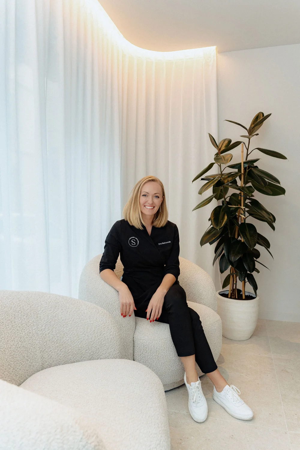 Two Smitasmile Barcelona dental professionals in black uniforms sitting in modern consultation area with white curtains, representing experienced team providing Advanced Smile Design services