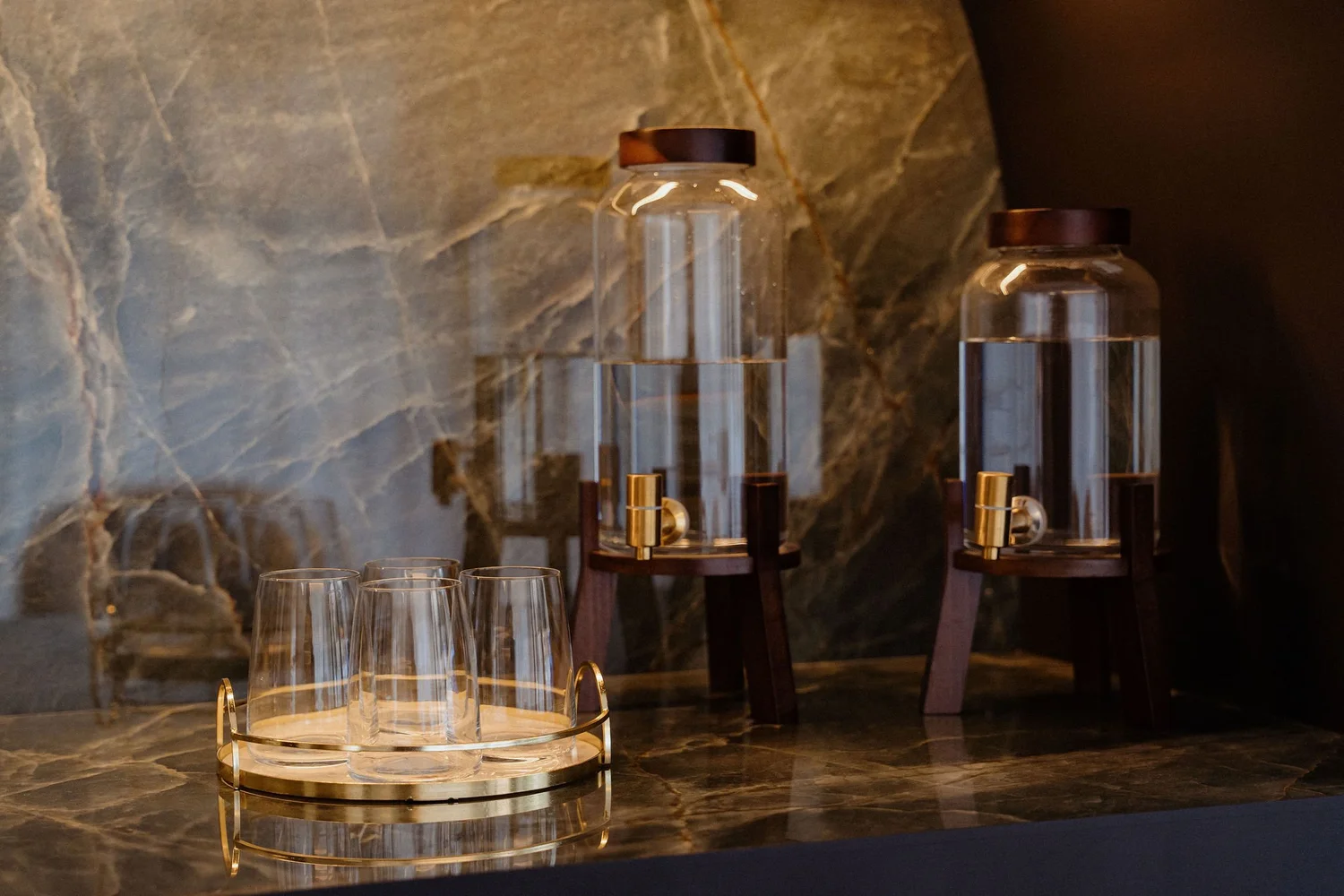 Smitasmile Barcelona water station with two elegant glass dispensers on marble counter, gold-accented taps, fresh water glasses - reflecting conscious dentistry commitment to patient care