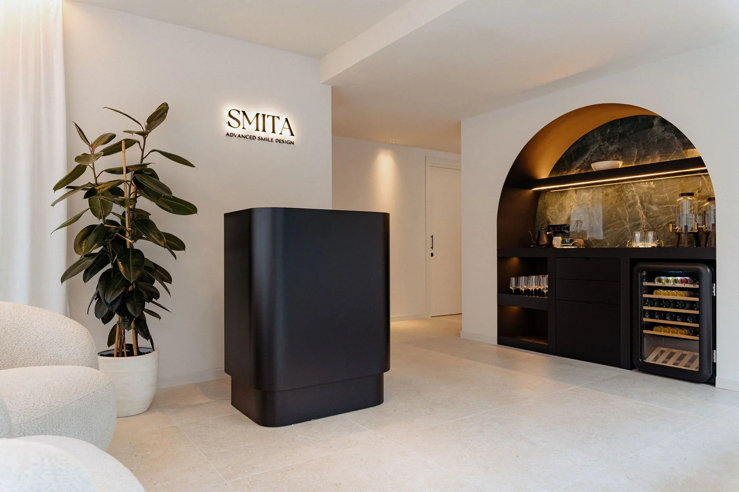 Smitasmile reception desk in Barcelona featuring modern black counter, comfortable beige seating, hospitality bar with premium glasses, green plants, and branded SMITA signage